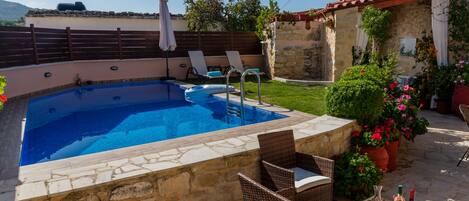 A swimming pool with stone walls, wicker chairs, and potted plants.