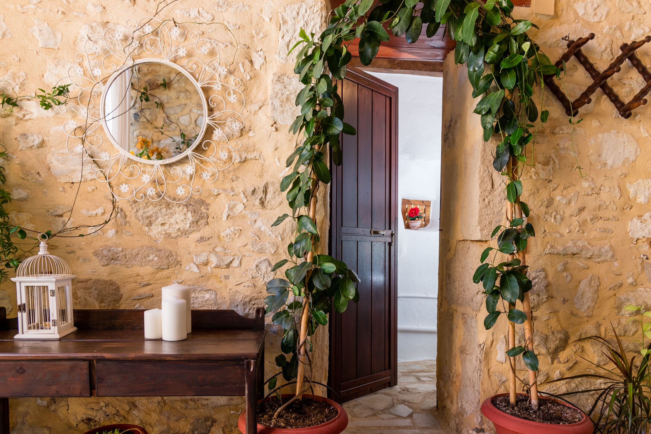 A rustic stone wall with a wooden door, a round mirror, and potted plants.