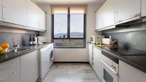 Une cuisine compacte équipée d’un lave-linge, d’un four à micro-ondes et d’un four traditionnel. Une fenêtre offre une vue sur les bâtiments et une tour.