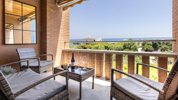 Un balcon agrémenté de meubles en osier, une table avec une bouteille et des verres, et une vue sur la mer.