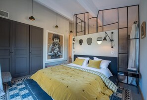 A bedroom with a large bed, a wardrobe, a wall-mounted artwork, and a bookshelf.