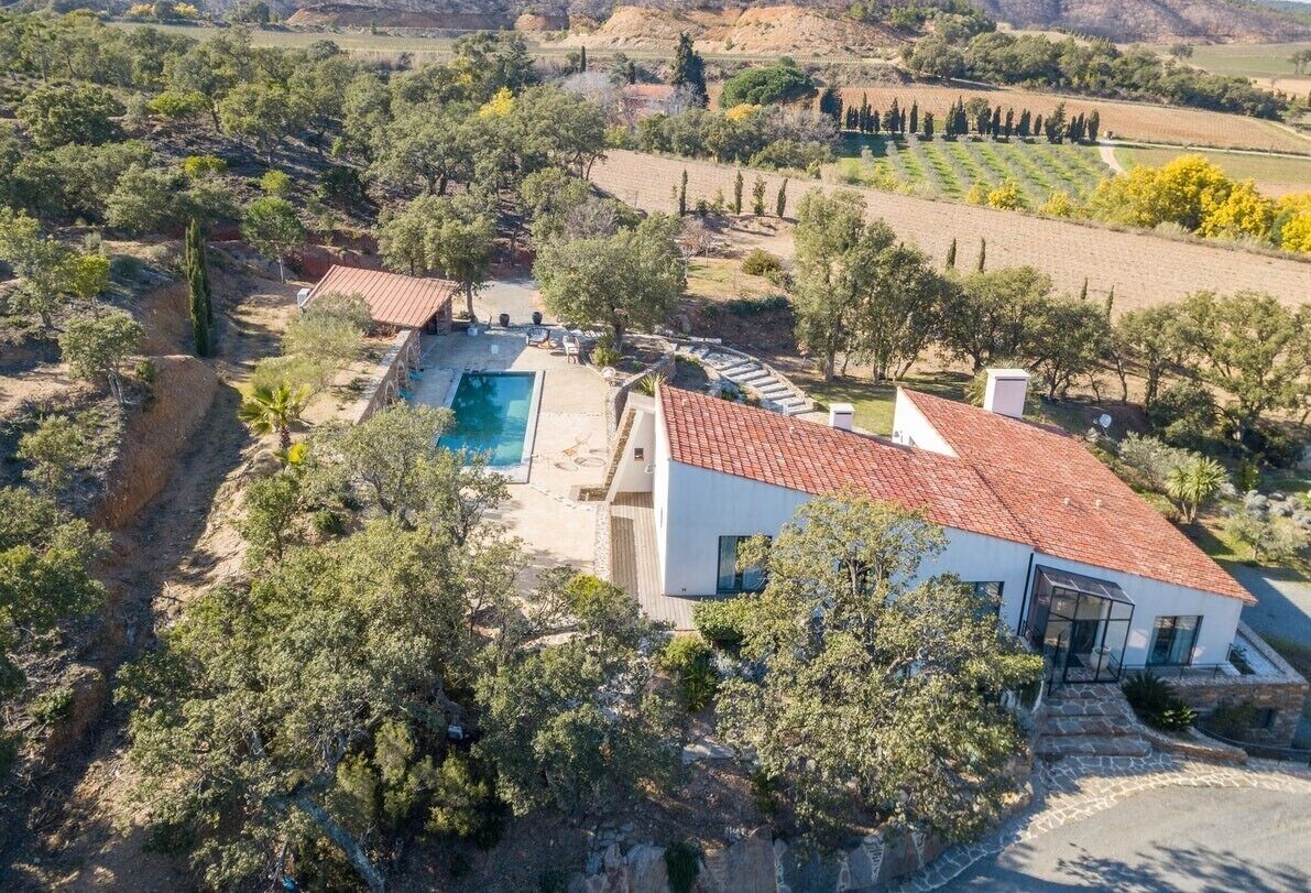 Une maison moderne avec une piscine, entourée d’arbres et de champs.