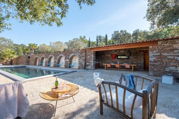 A pool area with stone walls, a covered seating area, and outdoor furniture.