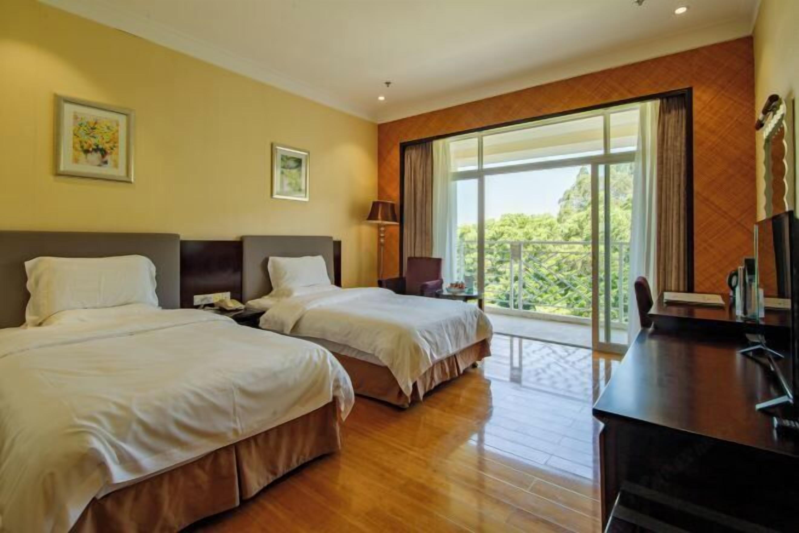 A hotel room with two beds, a desk, and a large window with a view of greenery.