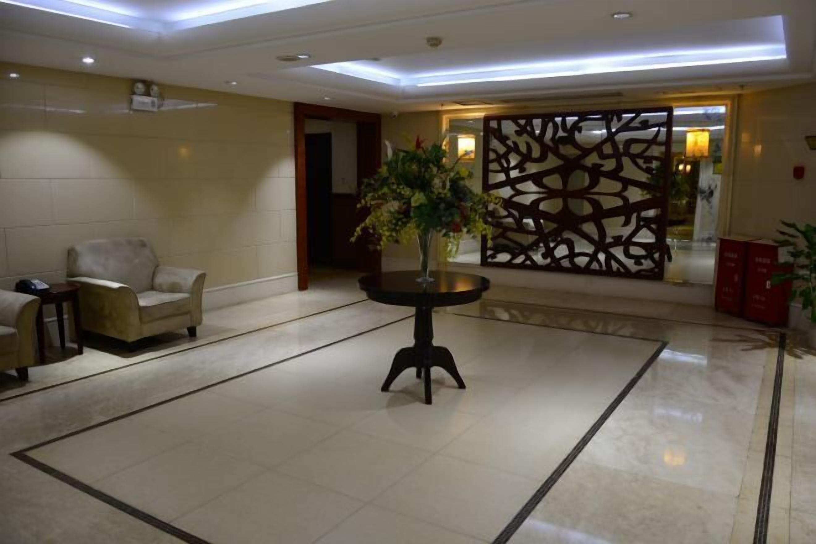 Un vestíbulo con una recepción, un sofá, una mesa con una planta y una pared decorativa.