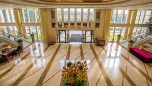 A spacious lobby with a marble floor, a central decorative plant, and a staircase on the right.