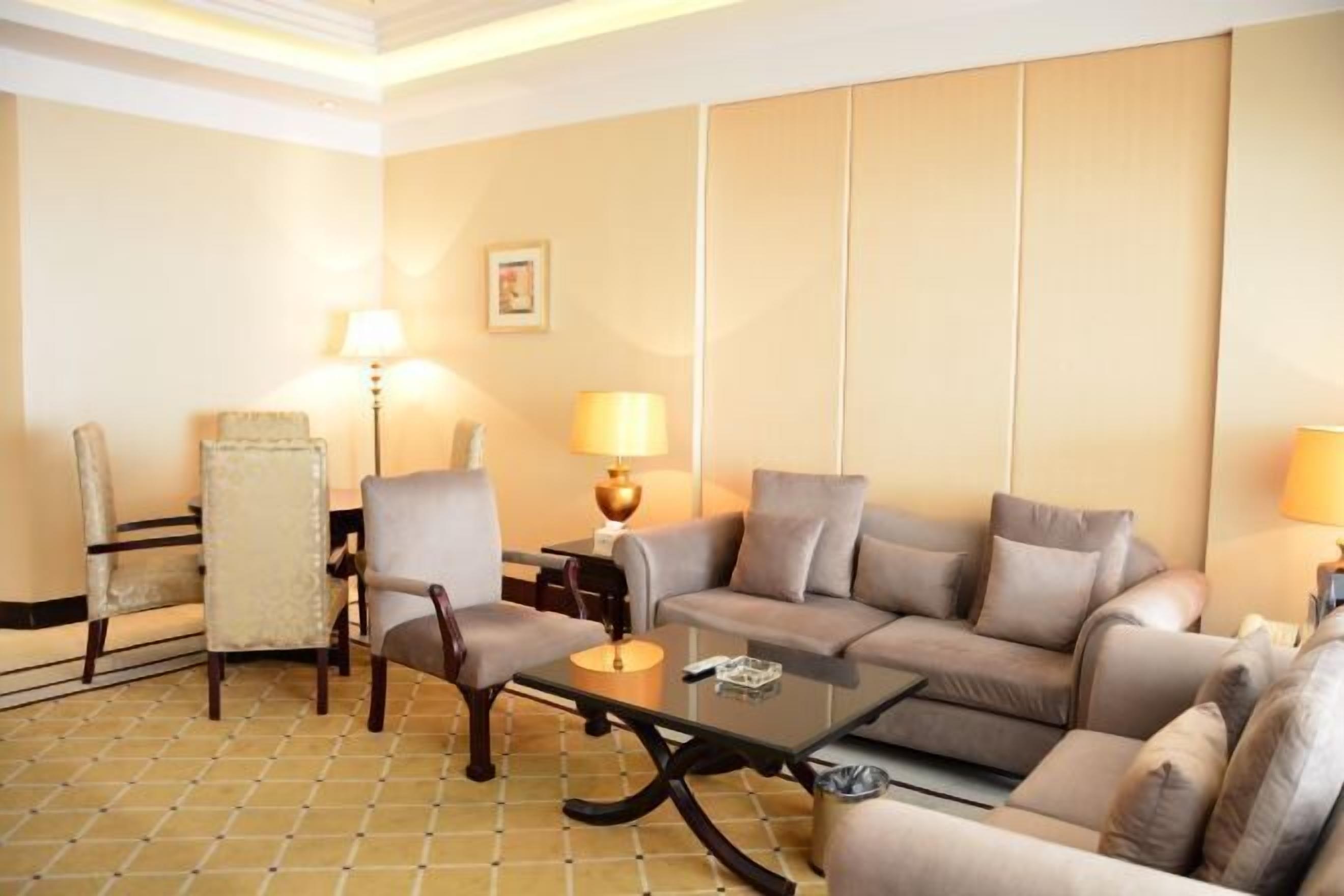 A hotel room with a sofa set, two armchairs, a coffee table, and two lamps.