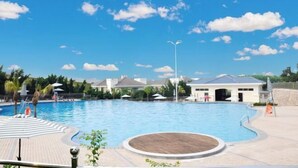 A swimming pool with a wooden deck, umbrellas, and lounge chairs.