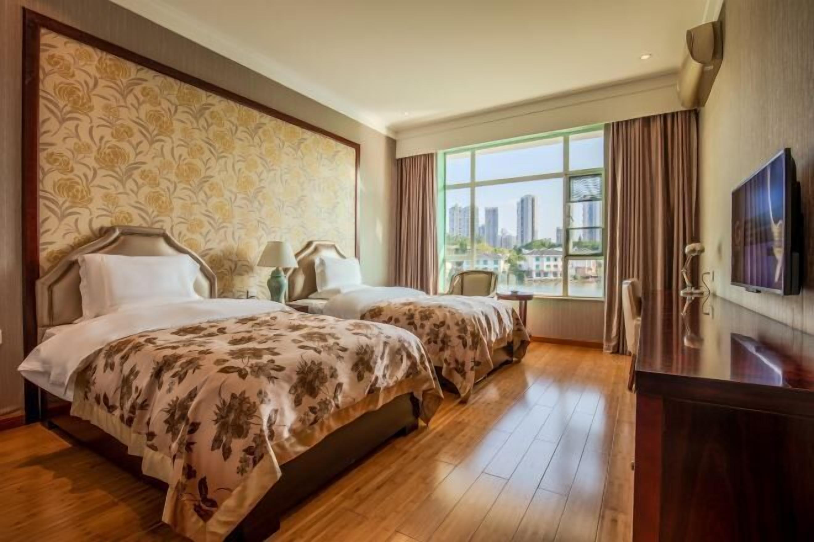 A hotel room with two beds, a large window with a city view, a TV, and a desk.