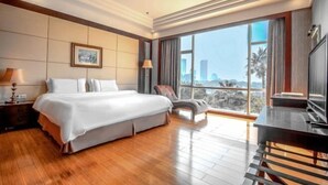 A spacious hotel room with a large bed, a chair, a desk, and a view of the cityscape.