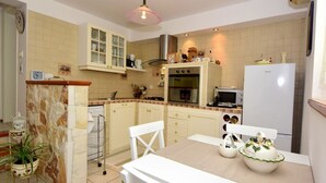 A kitchen with a stone island, white cabinets, and a dining table with a white chair. There is a microwave, oven, and a refrigerator. - Cosy apartment for 2 guests with WIFI, pool, A/C, TV, terrace and pets allowed (Solin)