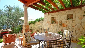 An outdoor patio with a stone wall, a round table, and metal chairs. - Cosy apartment for 2 guests with WIFI, pool, A/C, TV, terrace and pets allowed (Solin)