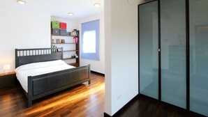 Una camera da letto moderna con un letto in legno, scaffali a muro con libri, un armadio e faretti a soffitto.