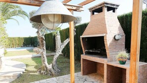 Barbecue in mattoni con canna fumaria, circondato da un patio in pietra e una pergola in legno.