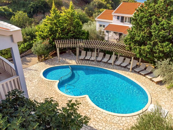 A swimming pool with a stone deck, surrounded by lounge chairs and a pergola.