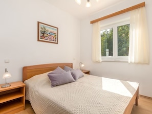 A bedroom with a bed, bedside tables, a lamp, a painting, and a window with a view of trees.