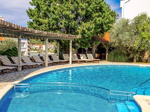 Una piscina con sillones de descanso, una pérgola y un árbol grande al fondo.