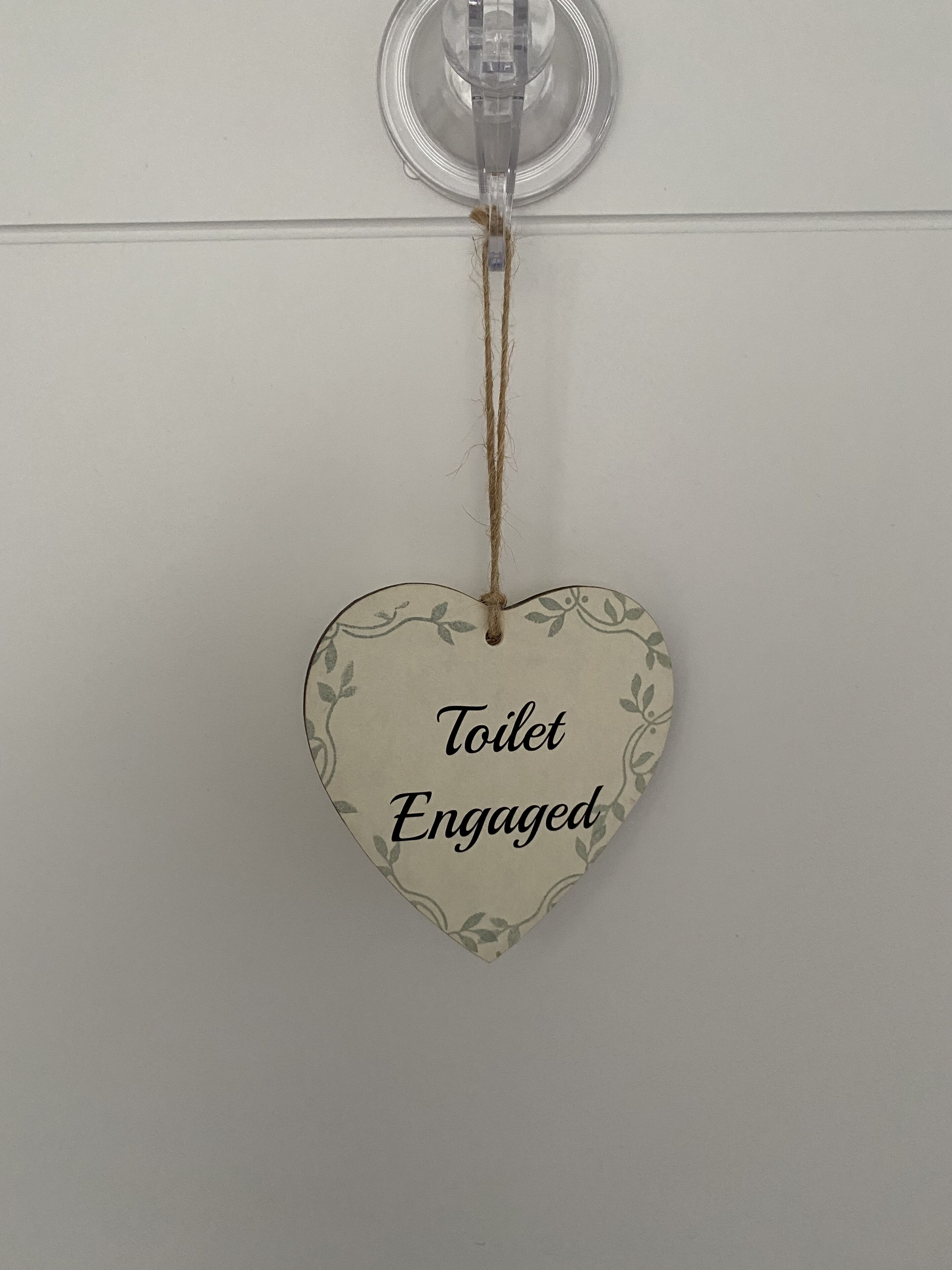 A heart-shaped sign with the text 'Toilet Engaged' hanging from a ceiling fixture.