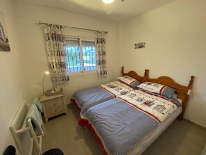 Un dormitorio con una cama de madera, una mesita de noche, una lámpara y una ventana con cortinas.