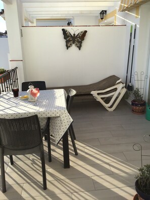 Un patio con una mesa y sillas, un adorno de mariposa en la pared y plantas en macetas.
