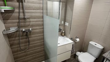 A modern bathroom with a glass-enclosed shower, a toilet, and a washing machine.
