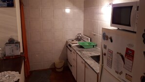 Cuina compacta amb rajoles blanques, microones, fogó a gas i prestatge verd per a la vaixella.