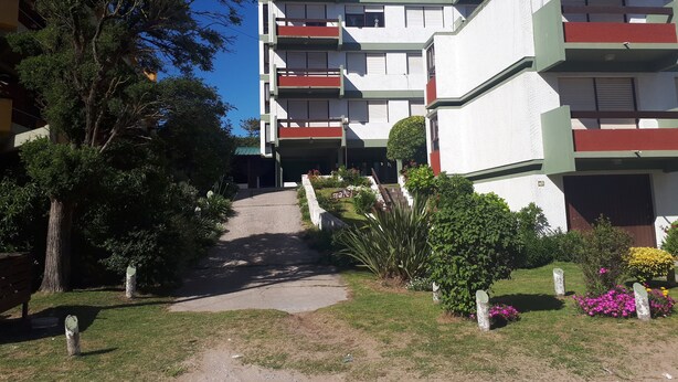 Un edifici de diversos pisos amb balcons, un camí empedrat i vegetació circumdant.