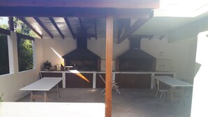 Un pati exterior amb una llar de pedra, dues taules i una estructura de pergola.