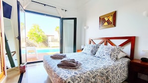 Ein Schlafzimmer mit einem Bett, einem Nachttisch, einem Gemälde und Blick auf einen Pool und Grünflächen.