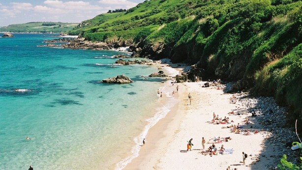 Una playa con agua turquesa cristalina, orilla de arena y colinas verdes exuberantes al fondo.