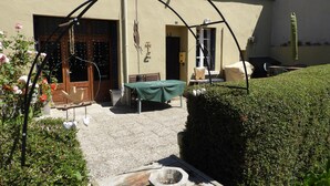 Un patio con una mesa de madera, una fuente de piedra y un mantel verde.