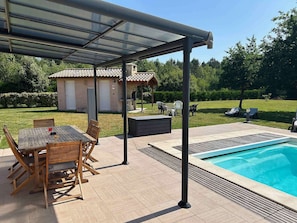 A covered outdoor area with a pool, wooden furniture, and a barbecue grill.