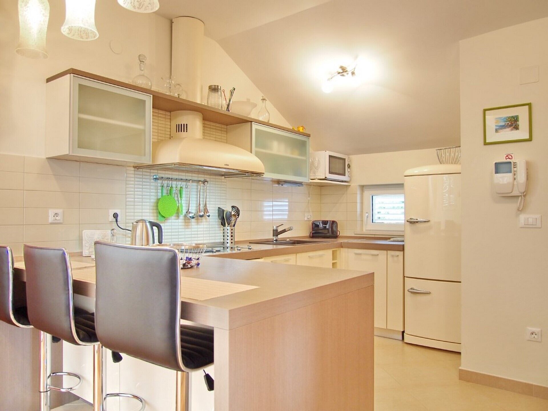 Een moderne keuken met een centraal eiland, barkrukken, een magnetron en een koelkast.