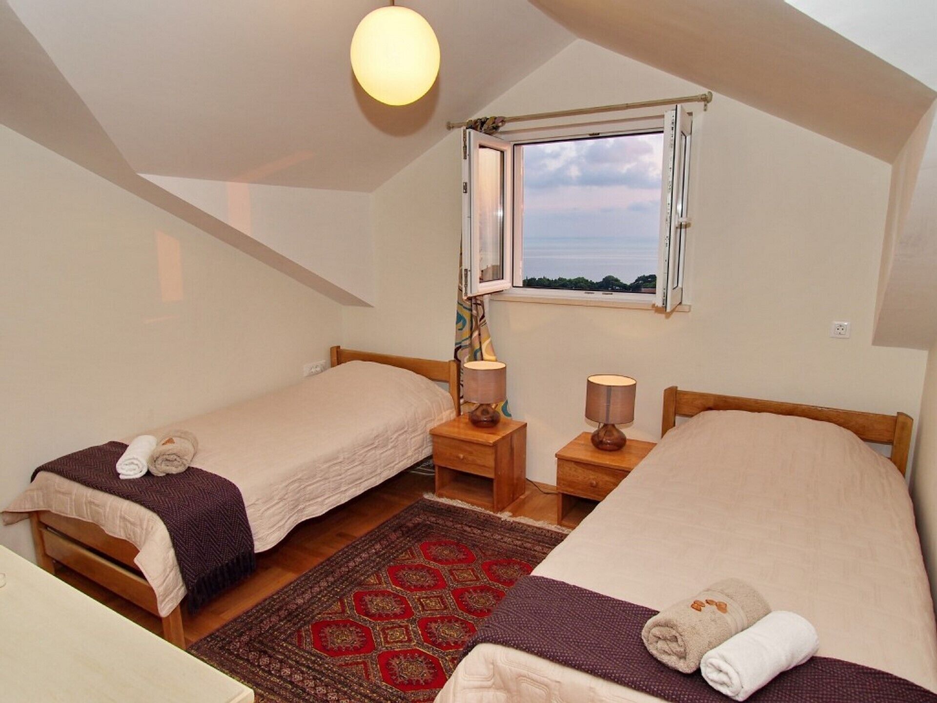 A small, cozy room with two single beds, a window with a view, a wooden floor, and a ceiling light.