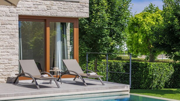 Un espace aménagé au bord de la piscine, comprenant deux chaises longues, une petite table et une porte vitrée donnant sur un patio abrité.
