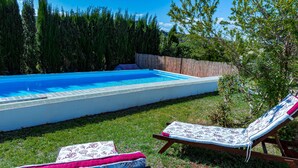 A swimming pool with two lounge chairs and a covered bench.