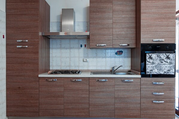A modern kitchen with wooden cabinets, a stainless steel range hood, a gas stove, a sink, and a black oven. - Welcome to Villa Mirta: Your Tranquil Retreat in Alghero (Alghero)