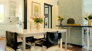 A modern kitchen with white cabinetry, a marble countertop, and a dining area with a white table and black chairs. - Magnificent Villa with private pool and garden (Sanremo)