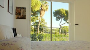 A bedroom with a bed, a painting on the wall, and a balcony with a view of trees and a fence. - Magnificent Villa with private pool and garden (Sanremo)