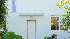 A white building with a door and windows, surrounded by potted plants with red flowers. - Magnificent Villa with private pool and garden (Sanremo)