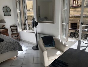 Una habitación con cama, una silla, una mesa, un ventilador y vistas al exterior.