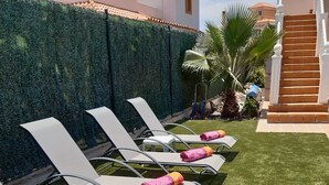 Fileira de gandules blanques amb tovalloles roses, disposades sobre un jardí ben cuidat, amb una tanca verda i palmeres al fons.