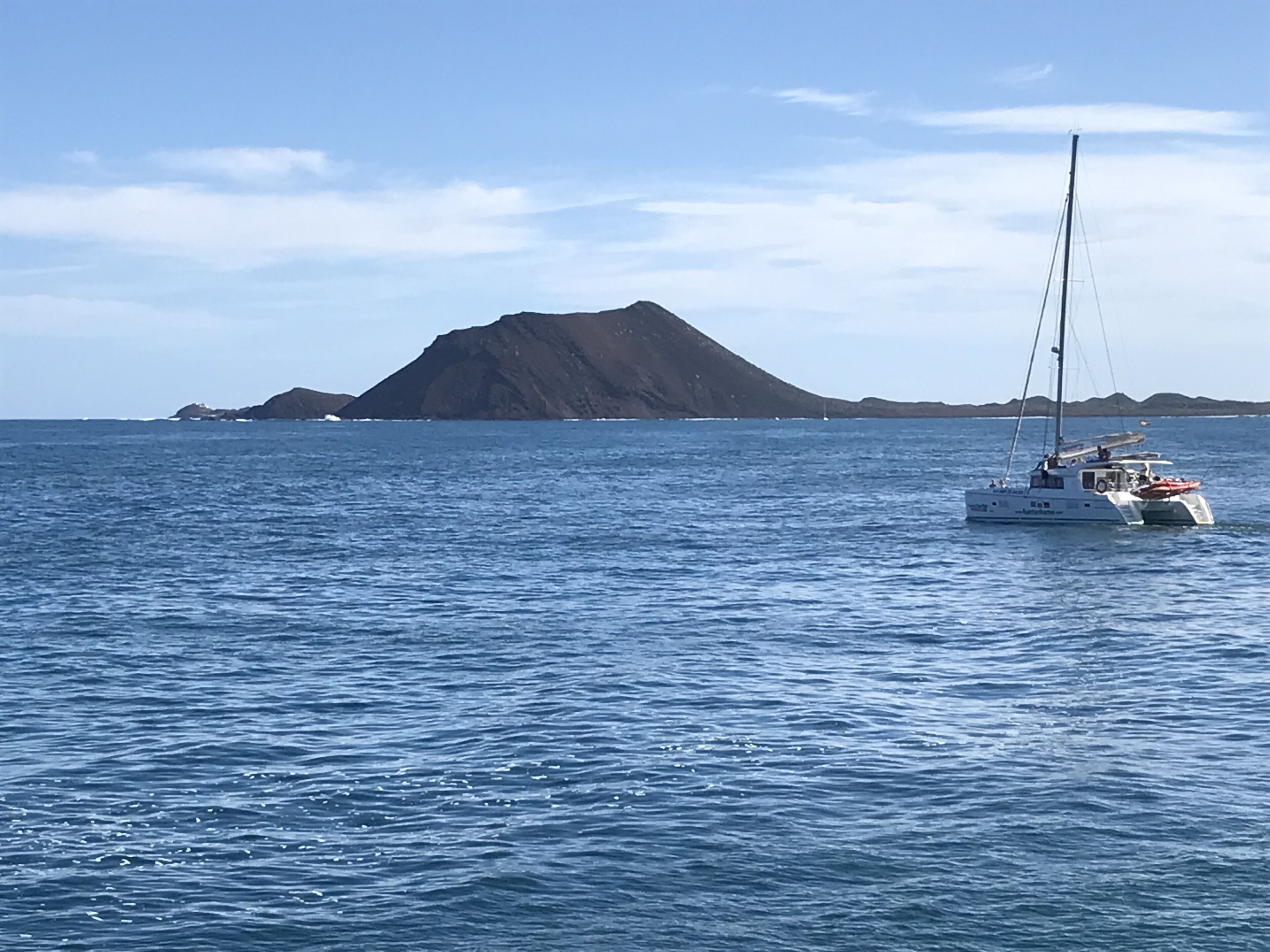 A sailboat on calm blue waters with a mountainous island in the background.