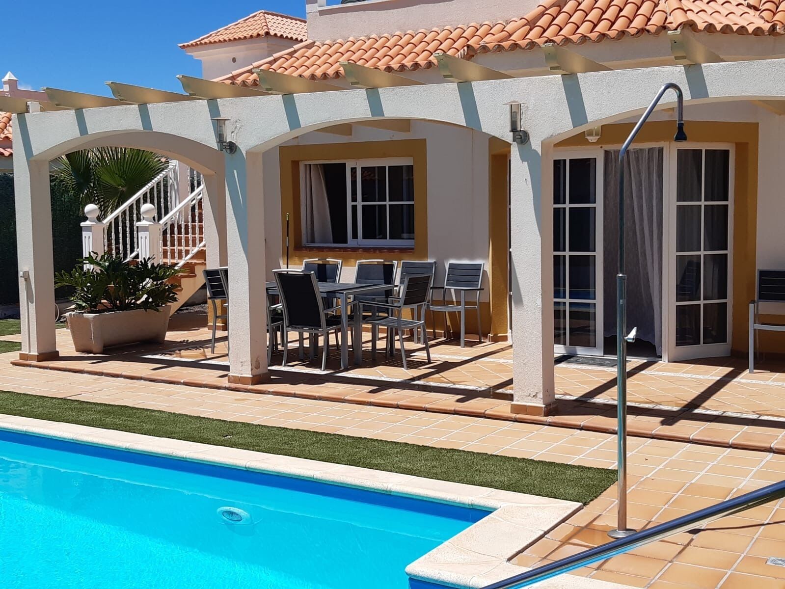 Zona junto a la piscina con un espacio de descanso cubierto, piscina y una escalera que lleva a un nivel superior.