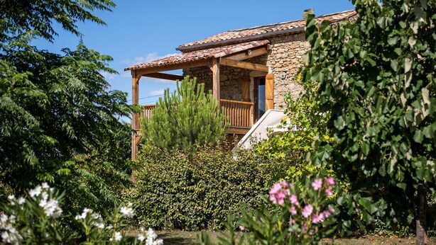 A stone building with a wooden balcony, surrounded by lush greenery and flowering plants. - La Magnanerie - Fantastic views, perfect base for the Ardeche and Chazzezac (Lablachère)