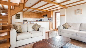 A spacious living area with a wooden staircase, two sofas with patterned cushions, a coffee table, and a kitchen in the background. - La Magnanerie - Fantastic views, perfect base for the Ardeche and Chazzezac (Lablachère)