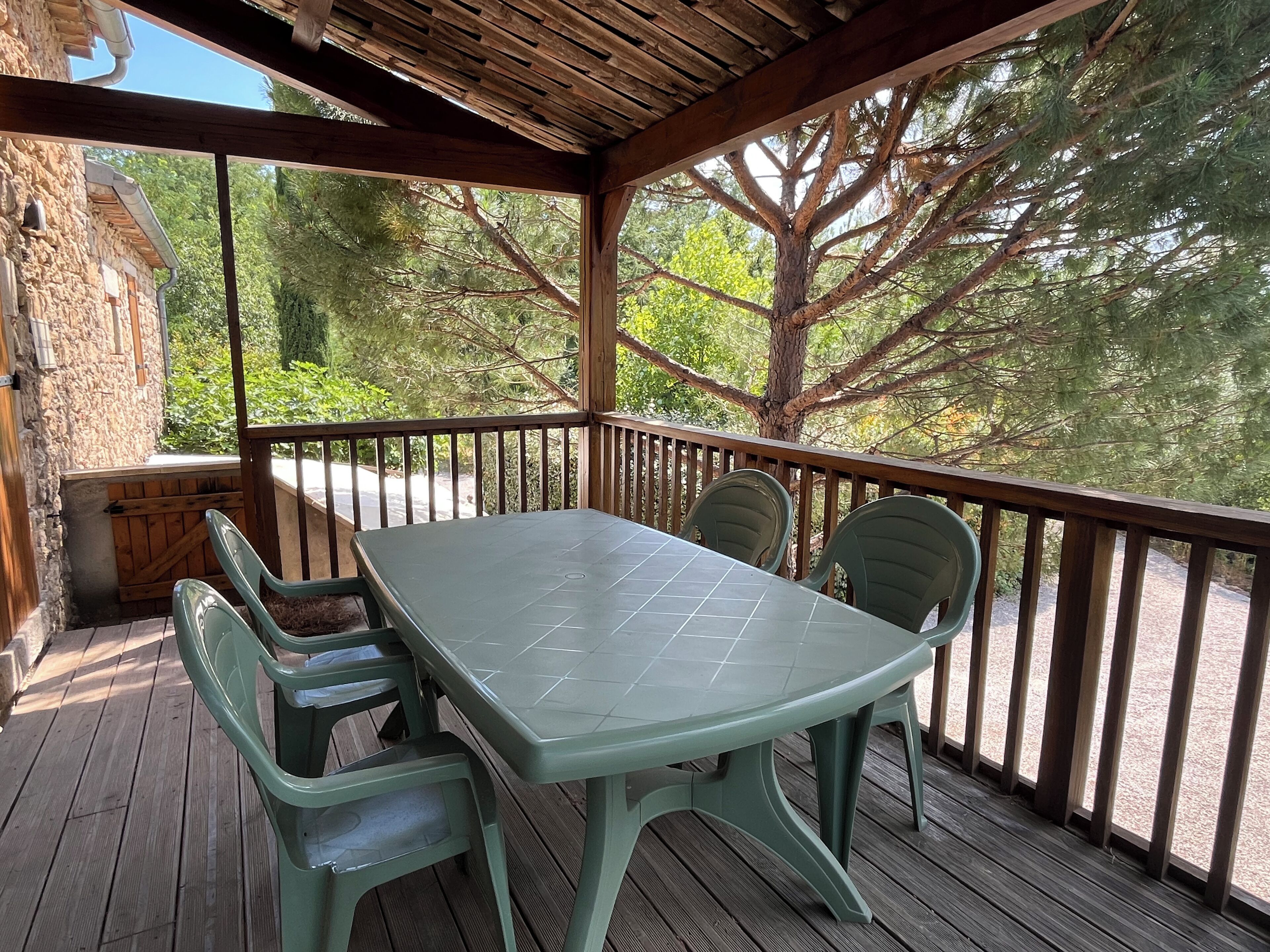 Een overdekt terras met een tafel en stoelen, omgeven door een houten vlonder en stenen muren.