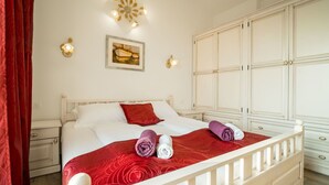 Een slaapkamer met een wit bed, rode beddengoed, een witte kledingkast en een decoratieve wandlamp.