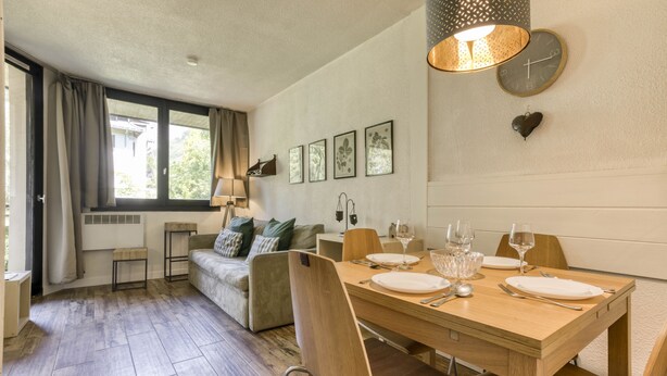 A dining area with a wooden table set for four, a sofa, and a window with curtains.