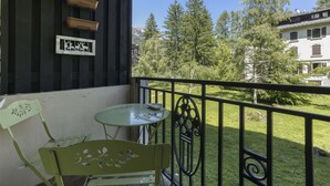 A balcony with a table and chairs, a metal railing, and a view of trees and buildings.
